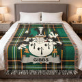 Plaid throw blanket with Gibbs family crest on a bed.
