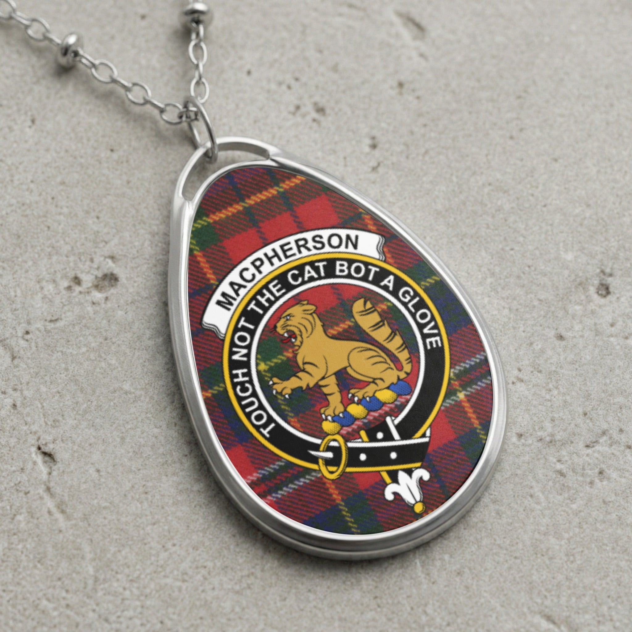 Macpherson clan crest with lion and motto on tartan background, silver necklace.