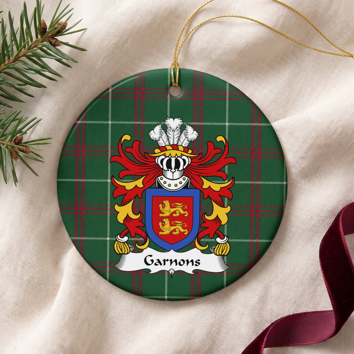 Garnons ornament on cream fabric beside evergreen and burgundy ribbon; two gold lions on a red shield enclosed by a blue border on Welsh national tartan.