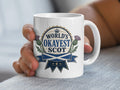 Mug with "World's Okayest Scot" text and Scottish thistle and flag.