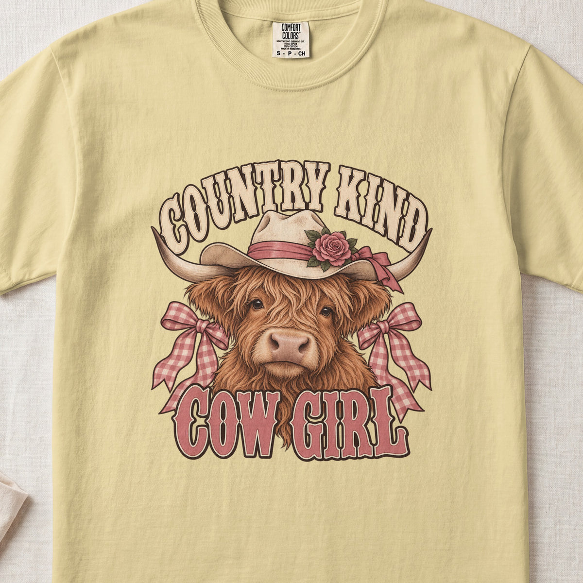 Country Kind Cow Girl Highland cow design on a Butter Comfort Colors 1717 T-shirt, flat lay