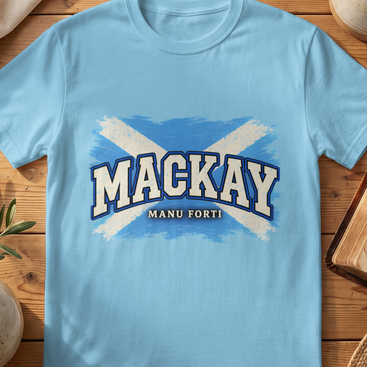 MacKay Scottish Saltire T-shirt in Sky, with distressed blue and cream flag and “Manu Forti” lettering.