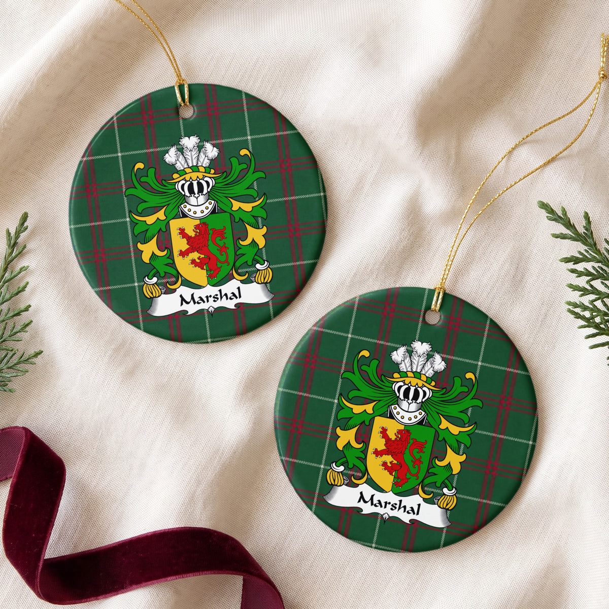 Two Marshal ornaments on cream fabric beside evergreen and burgundy ribbon, showing a red lion on a gold-and-green divided shield on Welsh National Tartan.