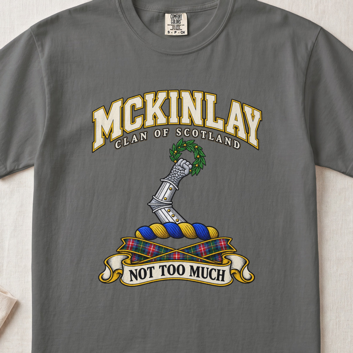 McKinlay Scottish clan T-shirt in Pepper, front view with an armored arm holding a green leafy wreath and motto banner.