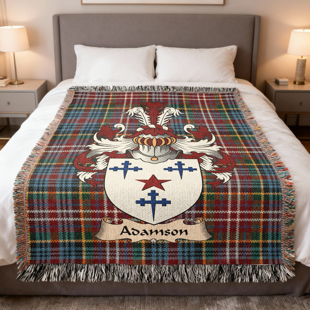 Adamson Scottish family crest woven blanket on a Caledonia tartan background, displayed on a bed