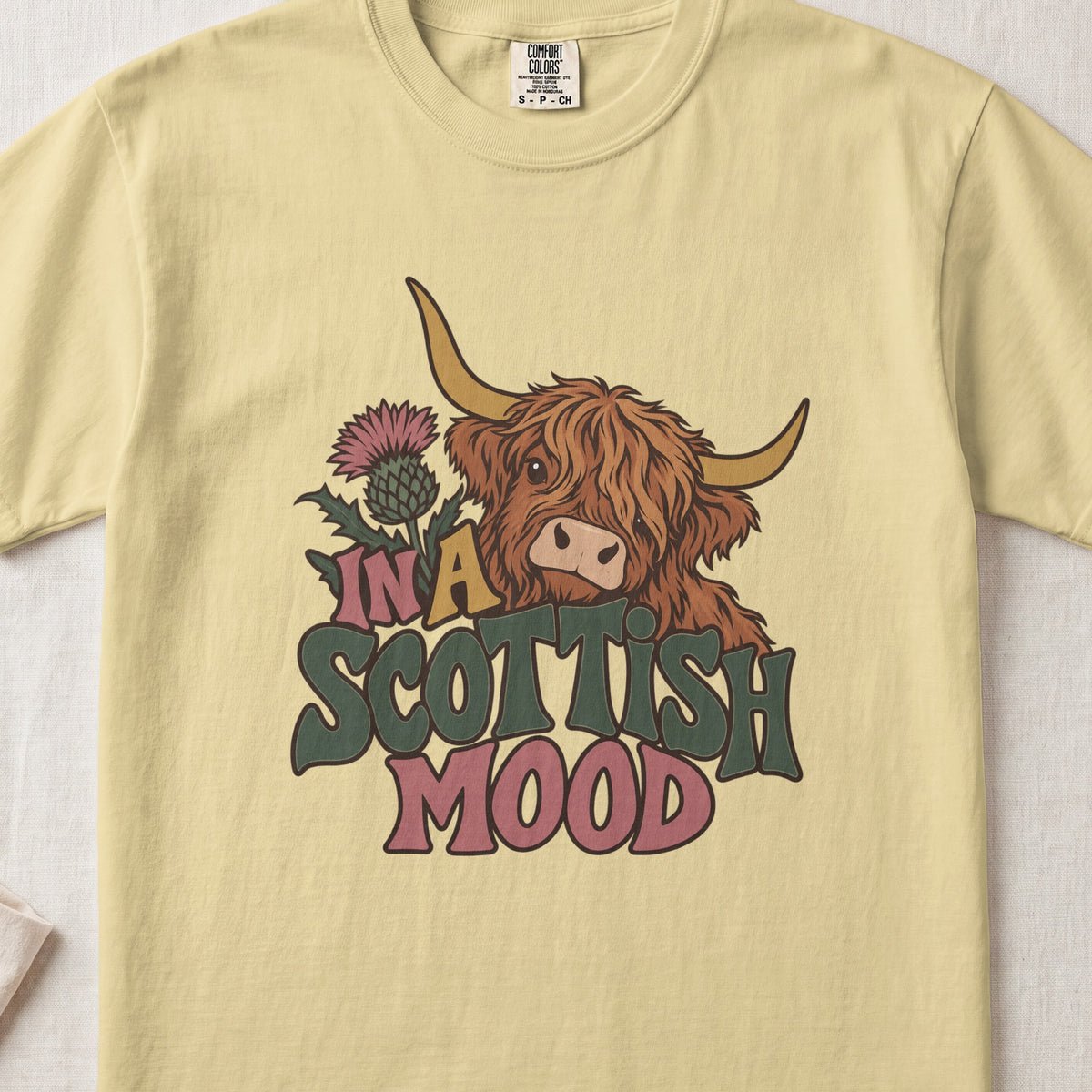 In a Scottish Mood Highland cow design on a Butter Comfort Colors 1717 T-shirt, flat lay
