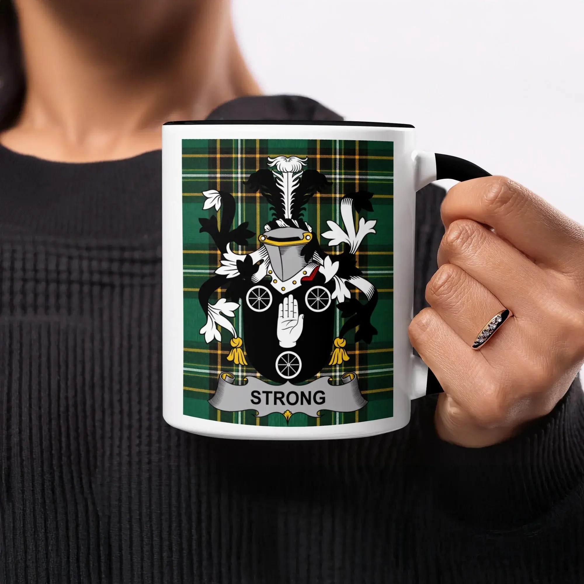 White mug with black handle, featuring the Strong family crest on a green plaid background.
