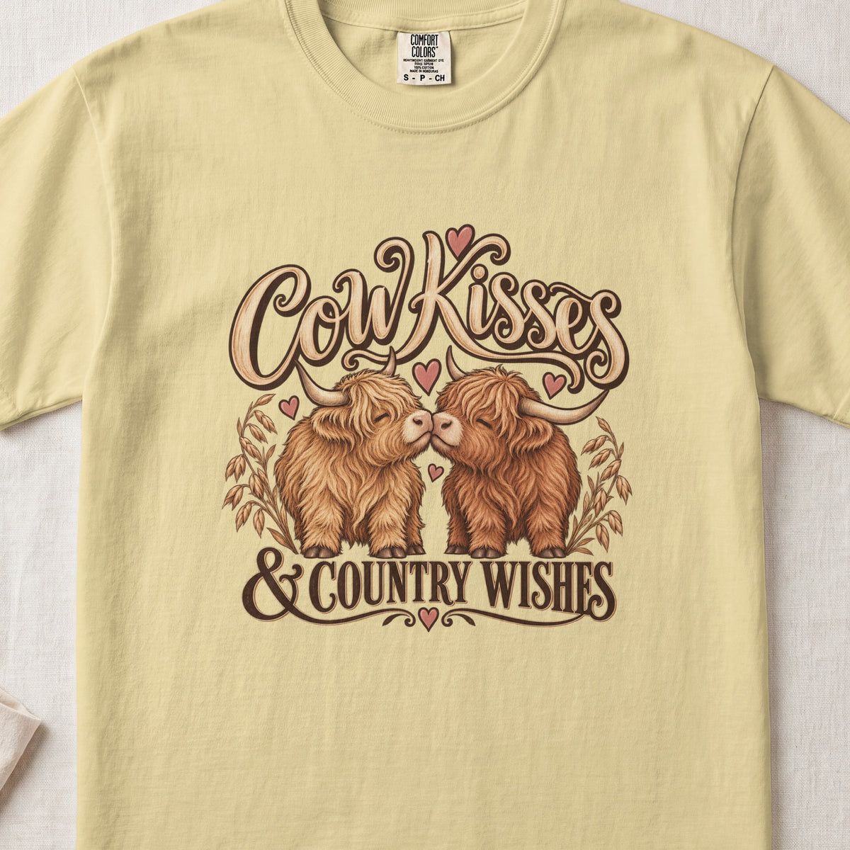 Cow Kisses & Country Wishes Highland cow design on a Butter Comfort Colors 1717 T-shirt, flat lay