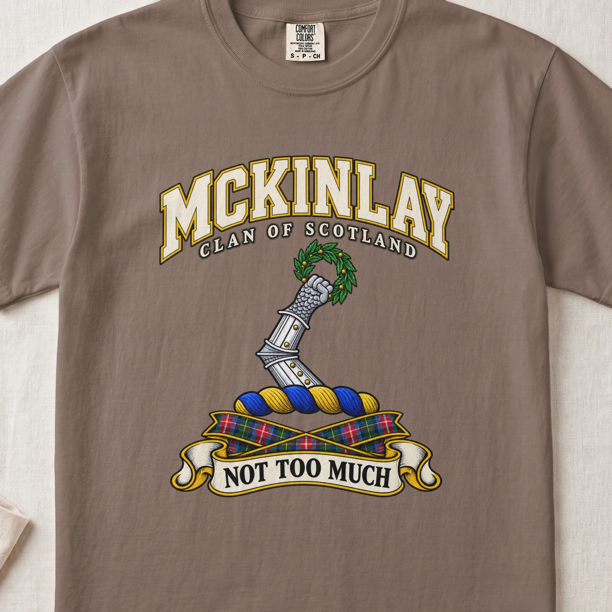 McKinlay Scottish clan T-shirt in Espresso, front view with an armored arm holding a green leafy wreath and motto banner.