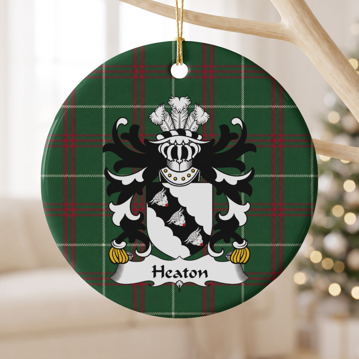Heaton ornament hanging from a pale wooden branch; three white bull heads on a scalloped black diagonal band across a white shield on Welsh national tartan.