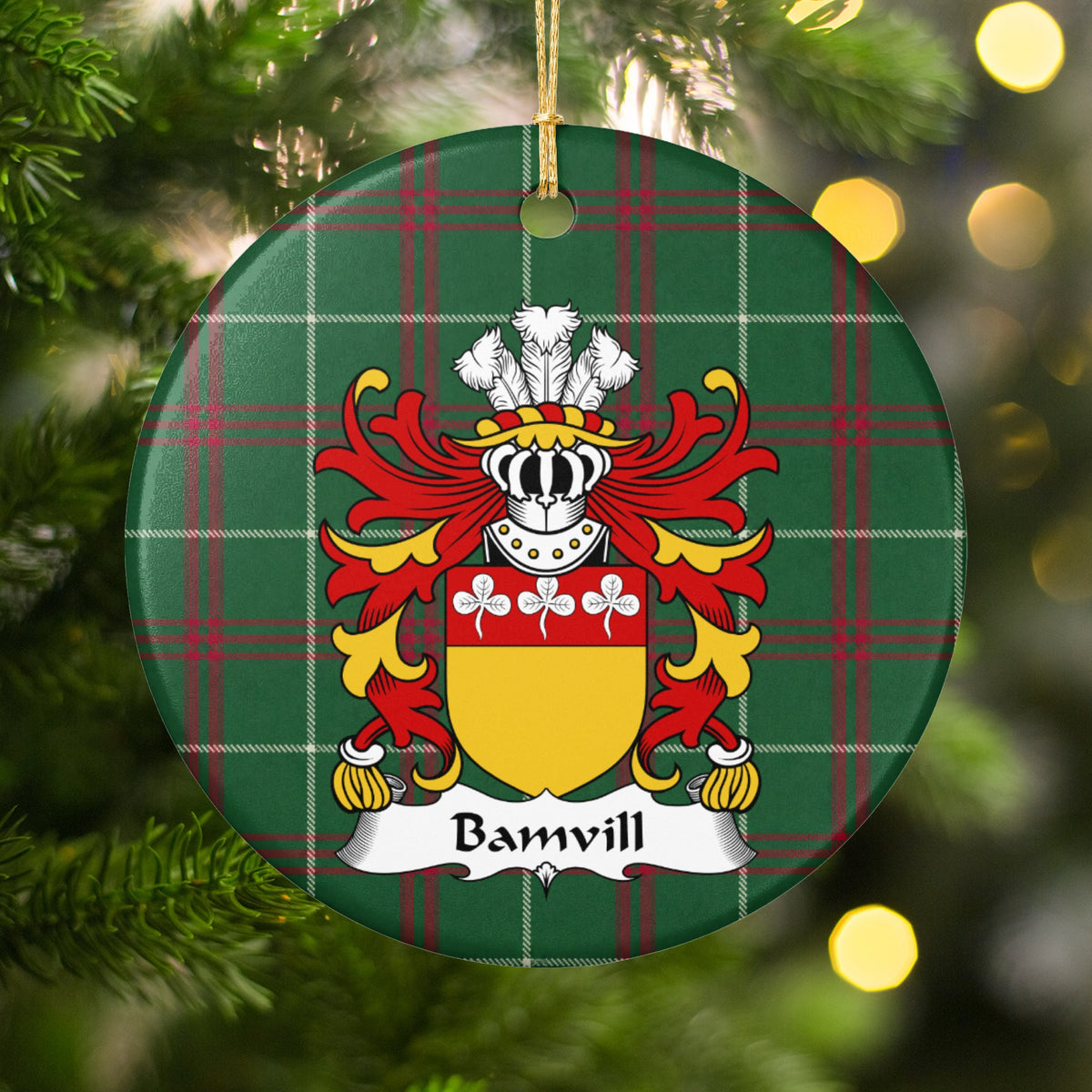 Bamvill ornament among Christmas tree branches and warm lights; three white trefoils on a red top band above a gold shield on Welsh national tartan.