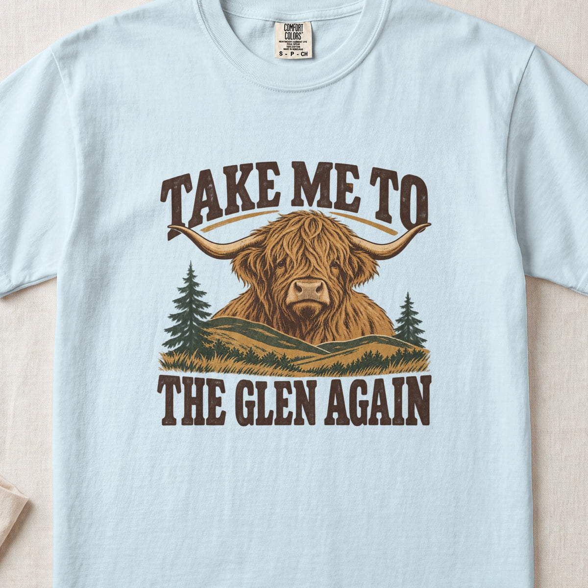 Take Me to the Glen Again Highland cow design on a Chambray Comfort Colors 1717 T-shirt, flat lay