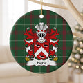 Herle ornament hanging from a pale wooden branch; three black-and-white ducks around a white chevron on a red shield on Welsh national tartan.