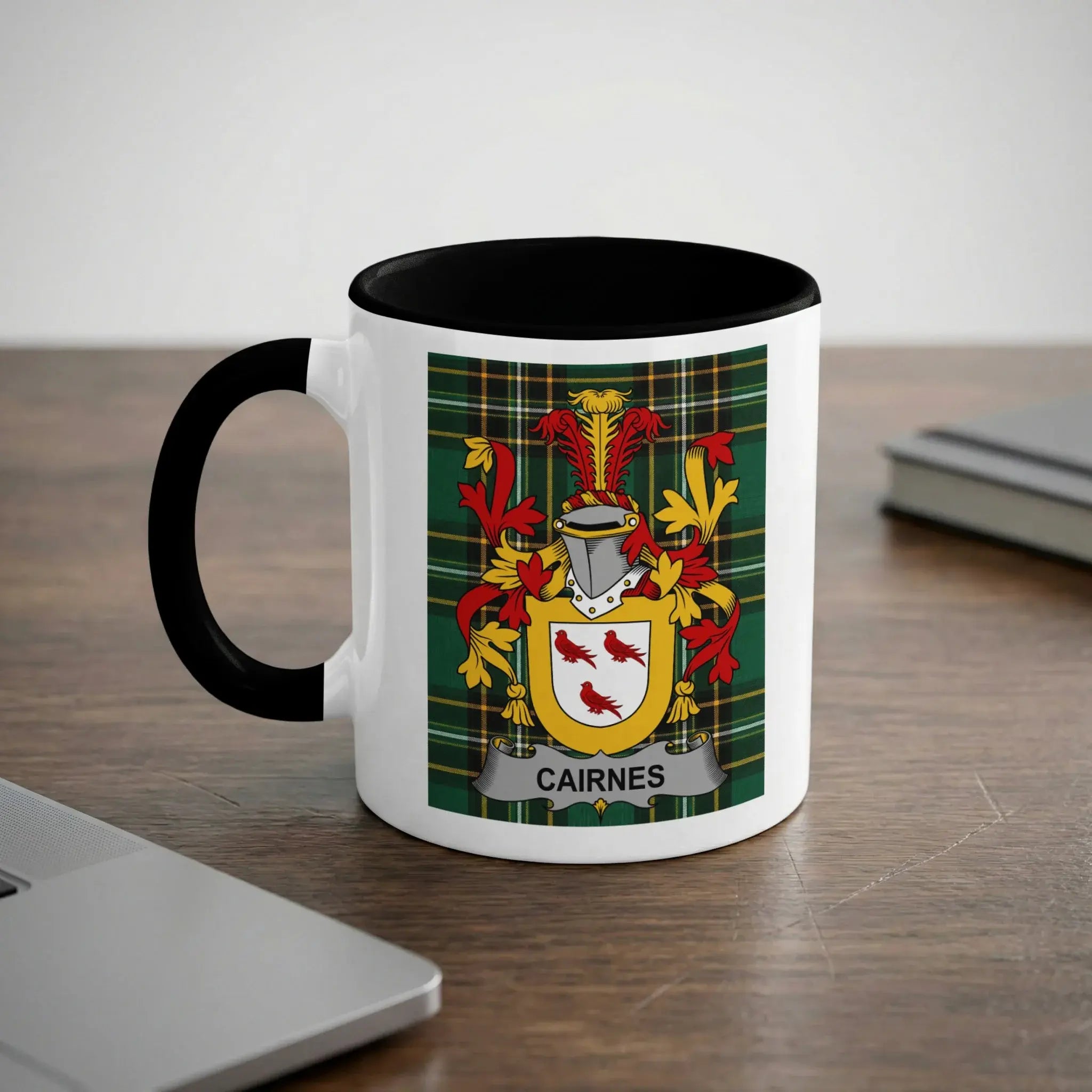 White mug with black rim featuring the "Cairnes" family crest on a plaid background.