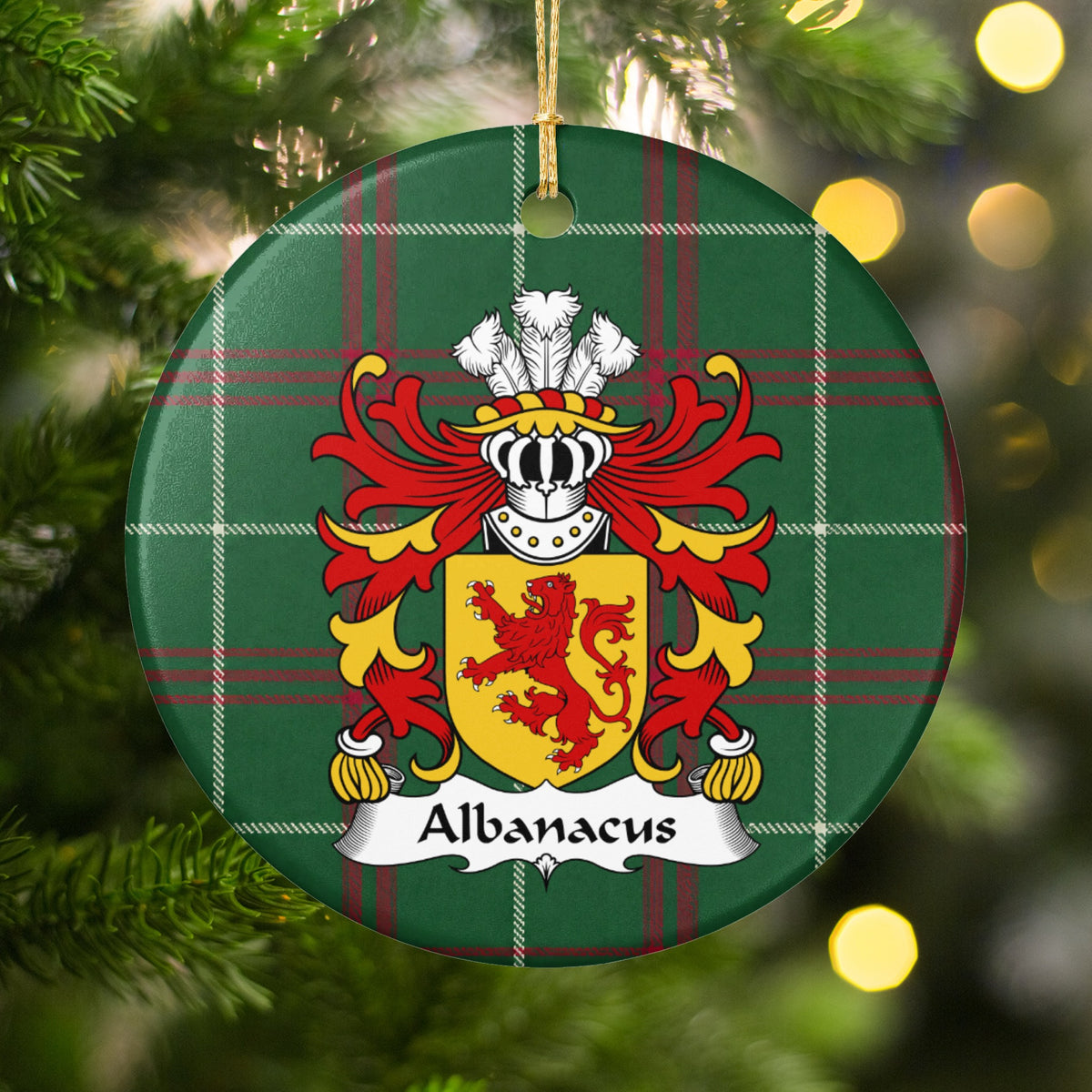 Albanacus family crest and surname on a round Welsh national tartan ornament, hanging by a gold cord among Christmas tree branches and warm golden lights.