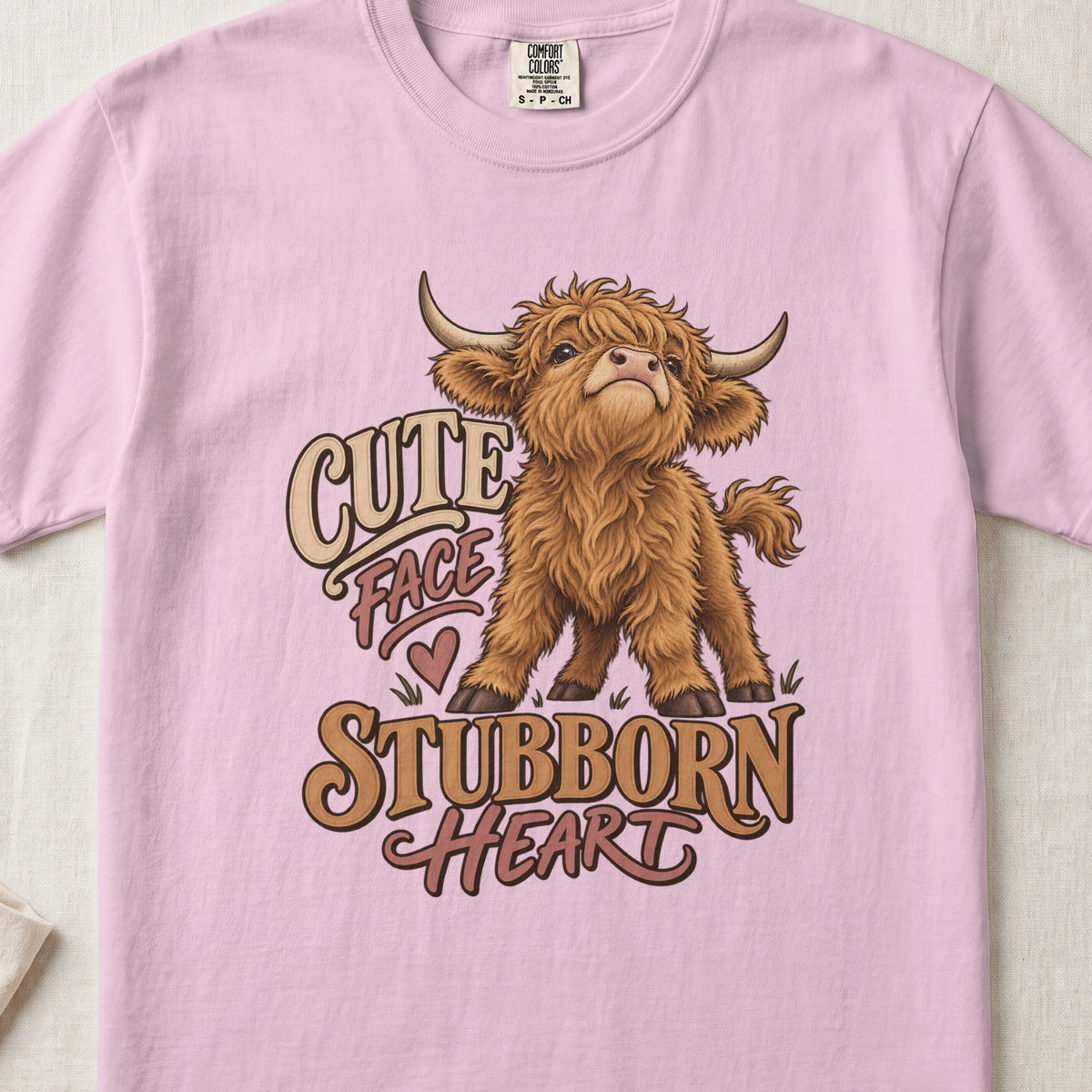 Cute Face, Stubborn Heart Highland cow design on a Blossom Comfort Colors 1717 T-shirt, flat lay