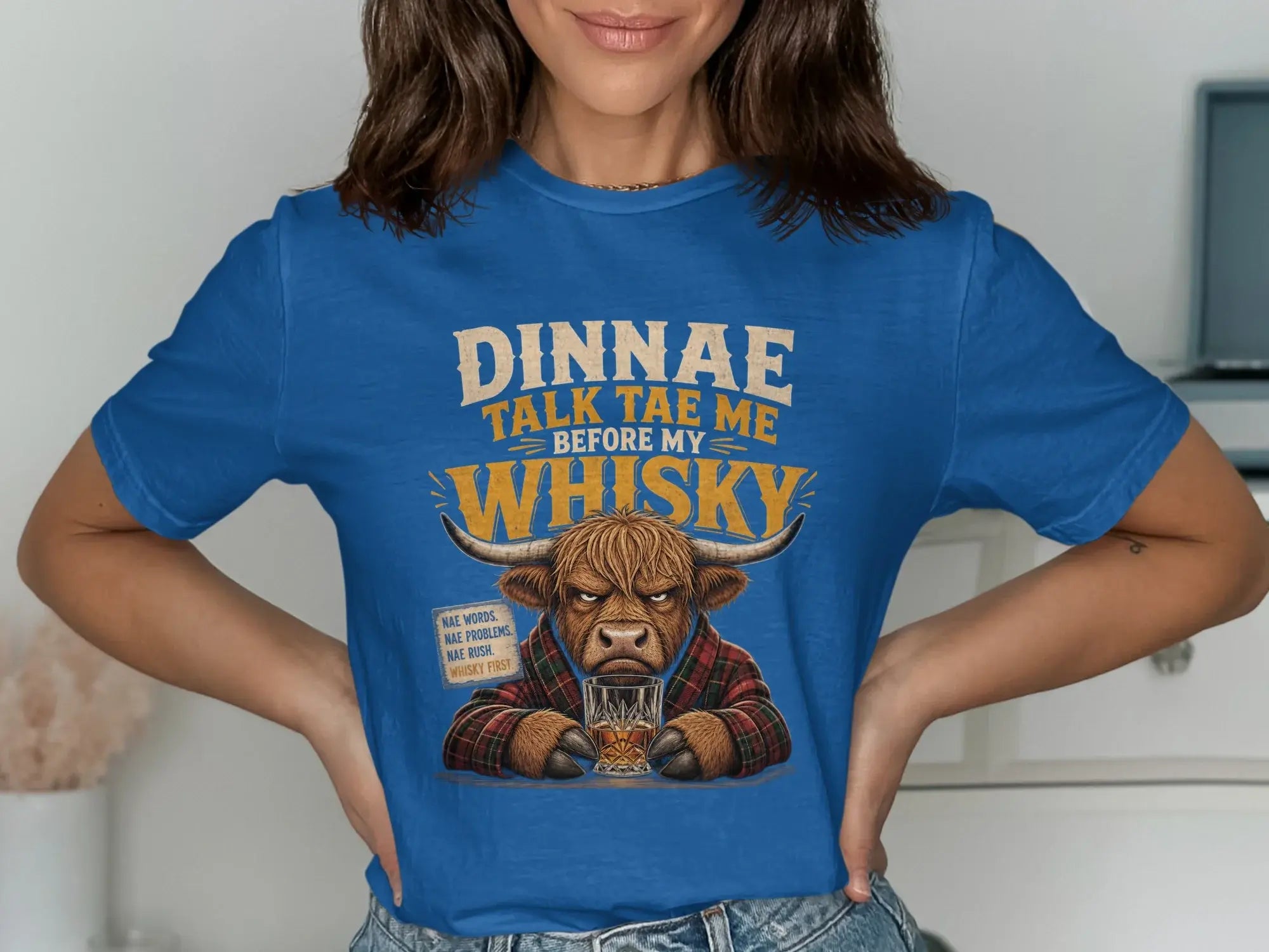 Highland cow in plaid shirt on blue t-shirt with "Dinnae talk tae me before my whisky" text.