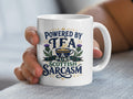 White mug with text "Powered by Tea & Pure Scottish Sarcasm" and thistle graphic.
