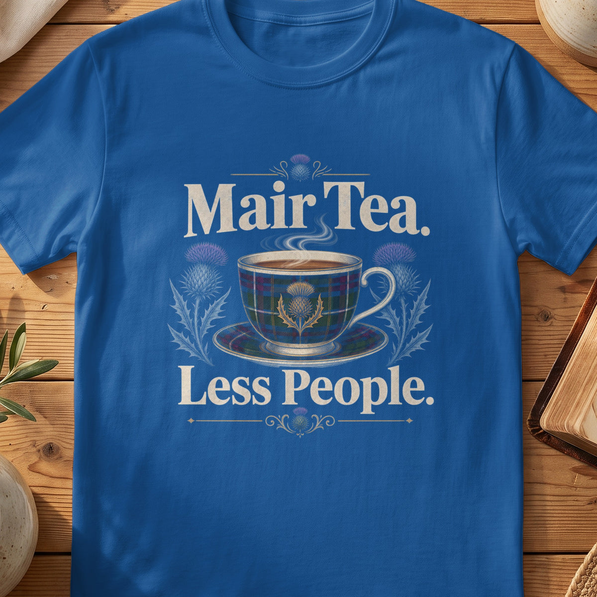 Blue t-shirt with text "Mair Tea. Less People." and a tartan teacup.