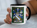 White mug with black rim featuring the Aland family crest on a tartan background.