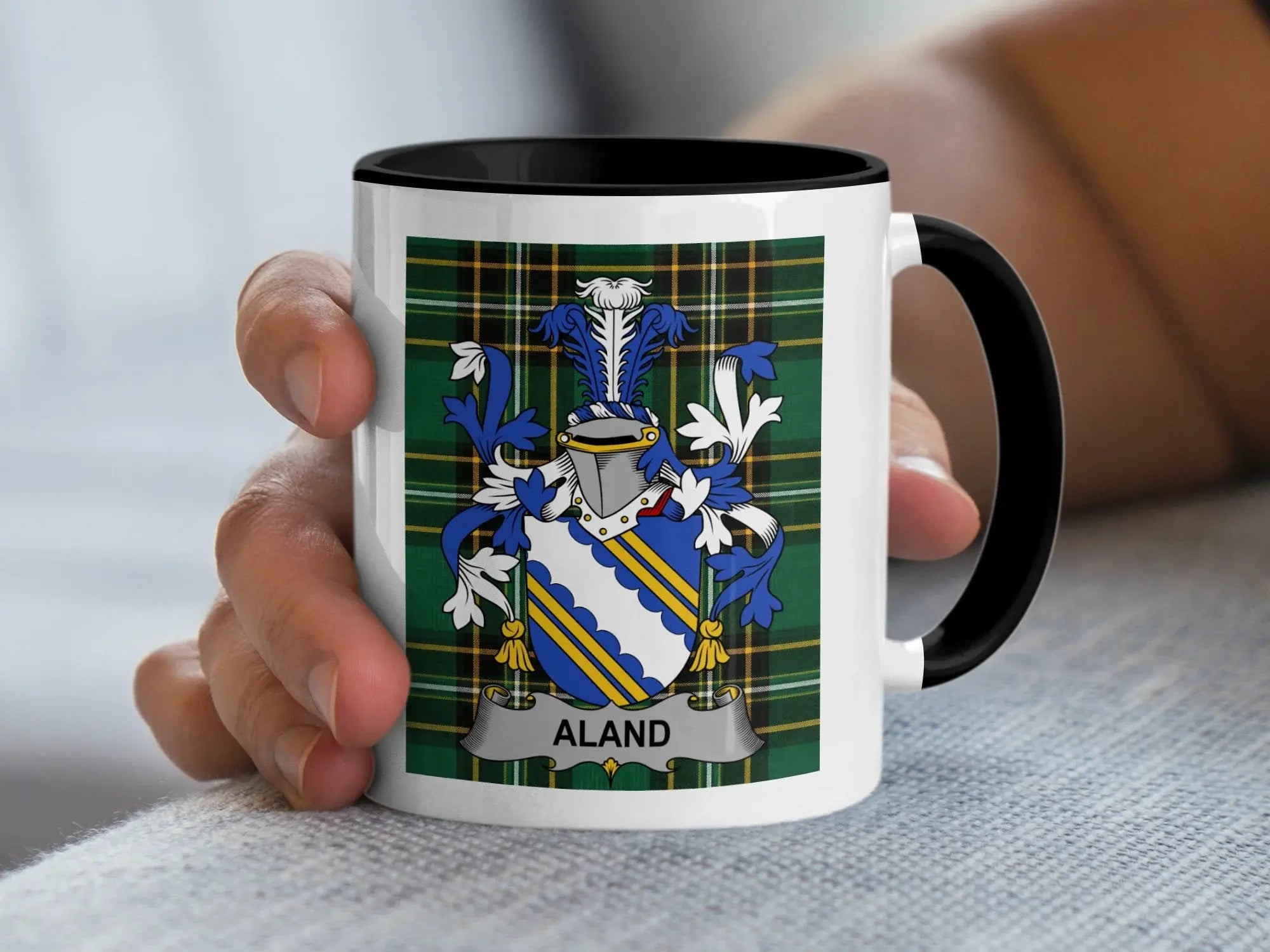 White mug with black rim featuring the Aland family crest on a tartan background.
