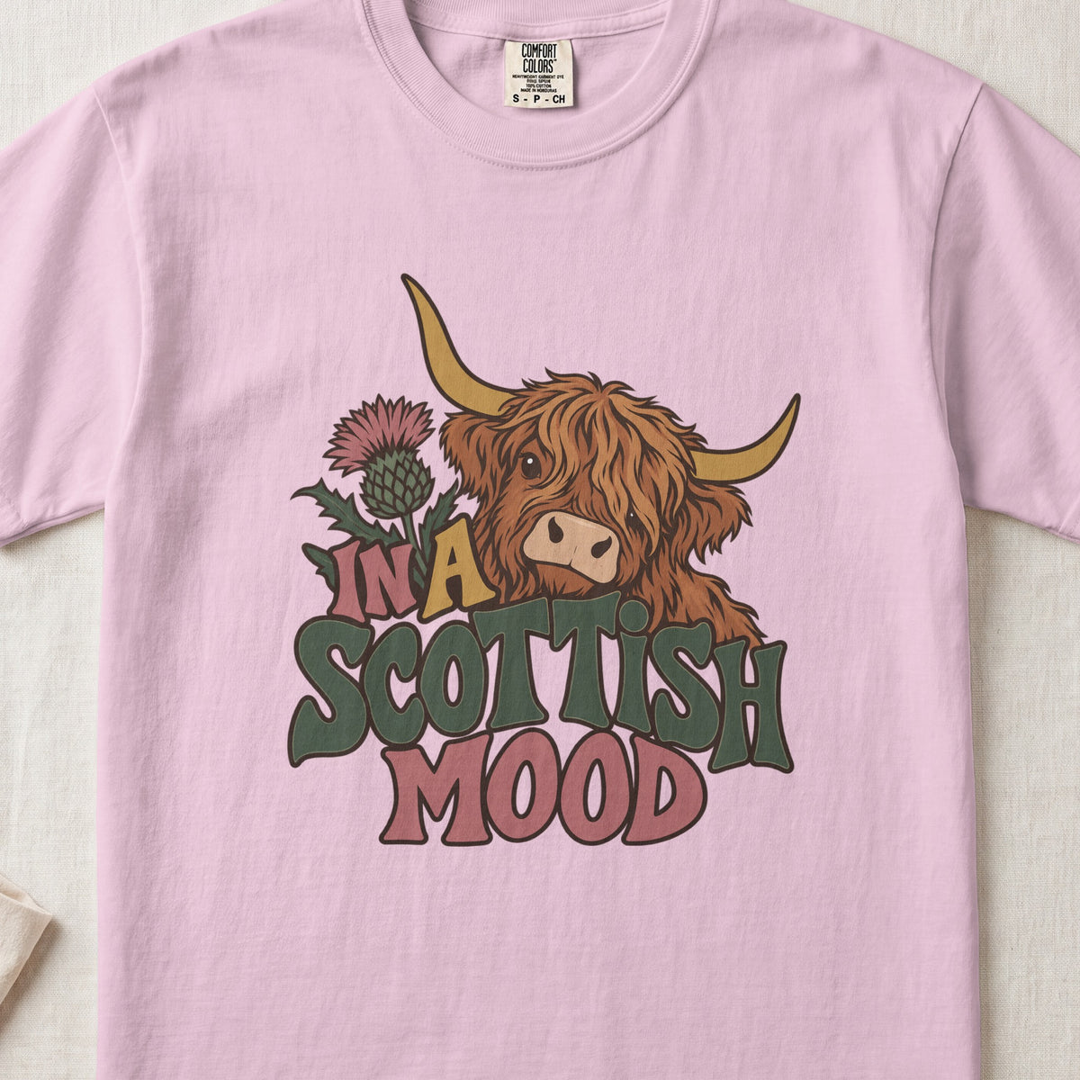 In a Scottish Mood Highland cow design on a Blossom Comfort Colors 1717 T-shirt, flat lay