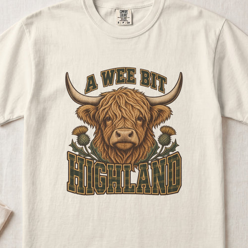 A Wee Bit Highland Highland cow design on an Ivory Comfort Colors 1717 T-shirt, flat lay
