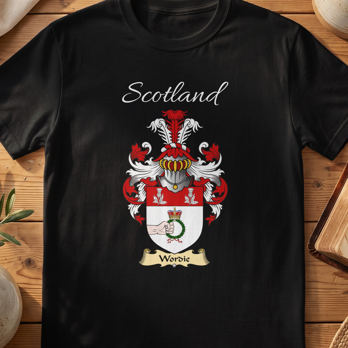 Black Wordie Scottish family crest T-shirt laid flat, showing “Scotland” above a red-and-silver shield with a leafy tree and heart detail.