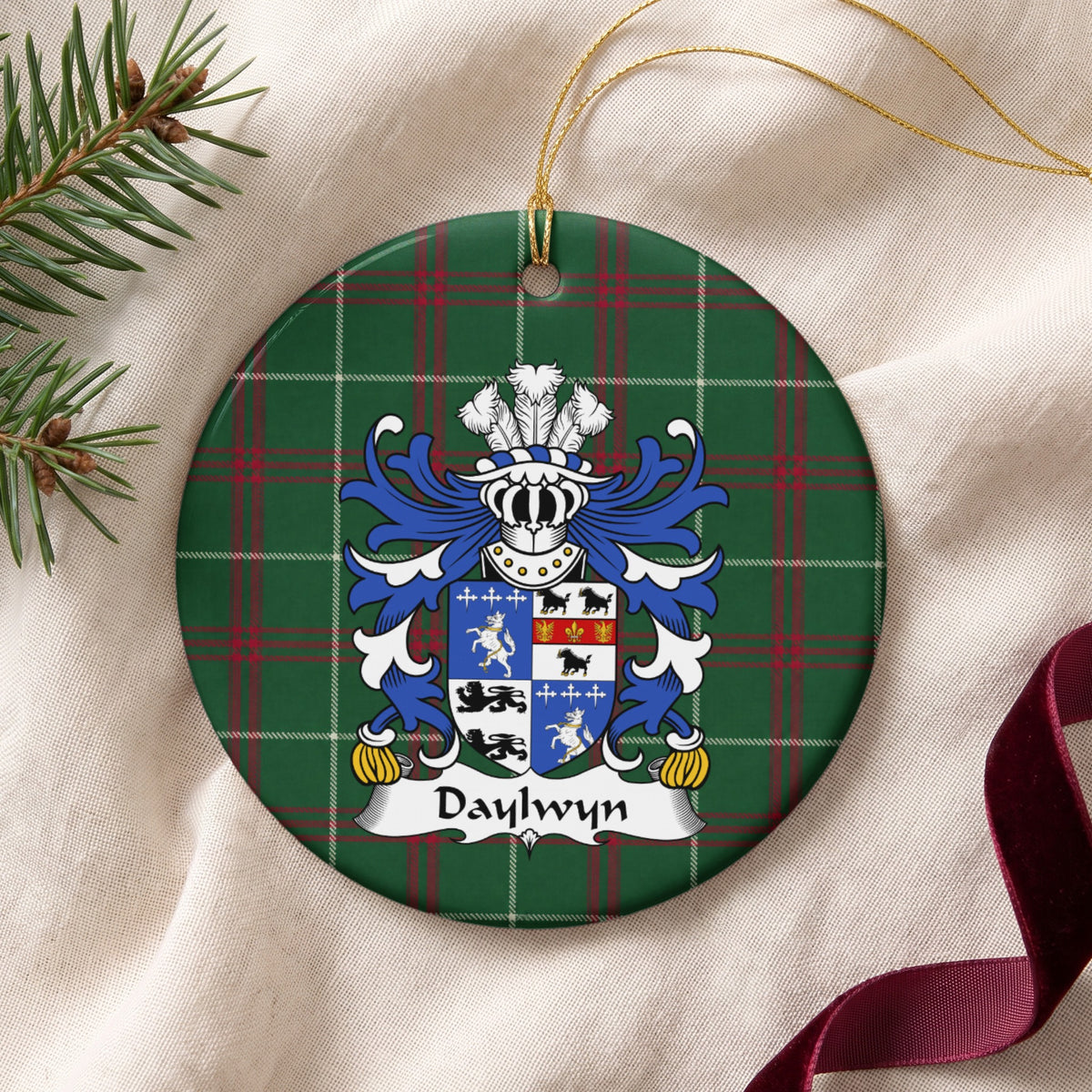 Daylwyn ornament on cream fabric with gold string, evergreen and burgundy ribbon; a quartered blue-and-white shield with lions, dark animals and small cross motifs.