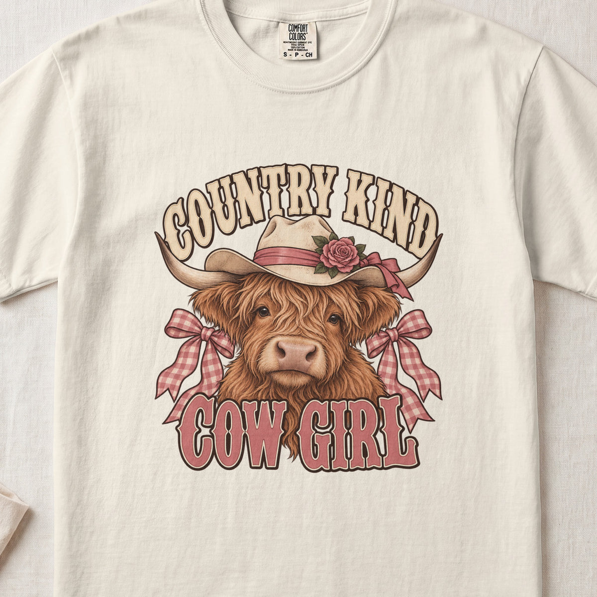 Country Kind Cow Girl Highland cow design on an Ivory Comfort Colors 1717 T-shirt, flat lay