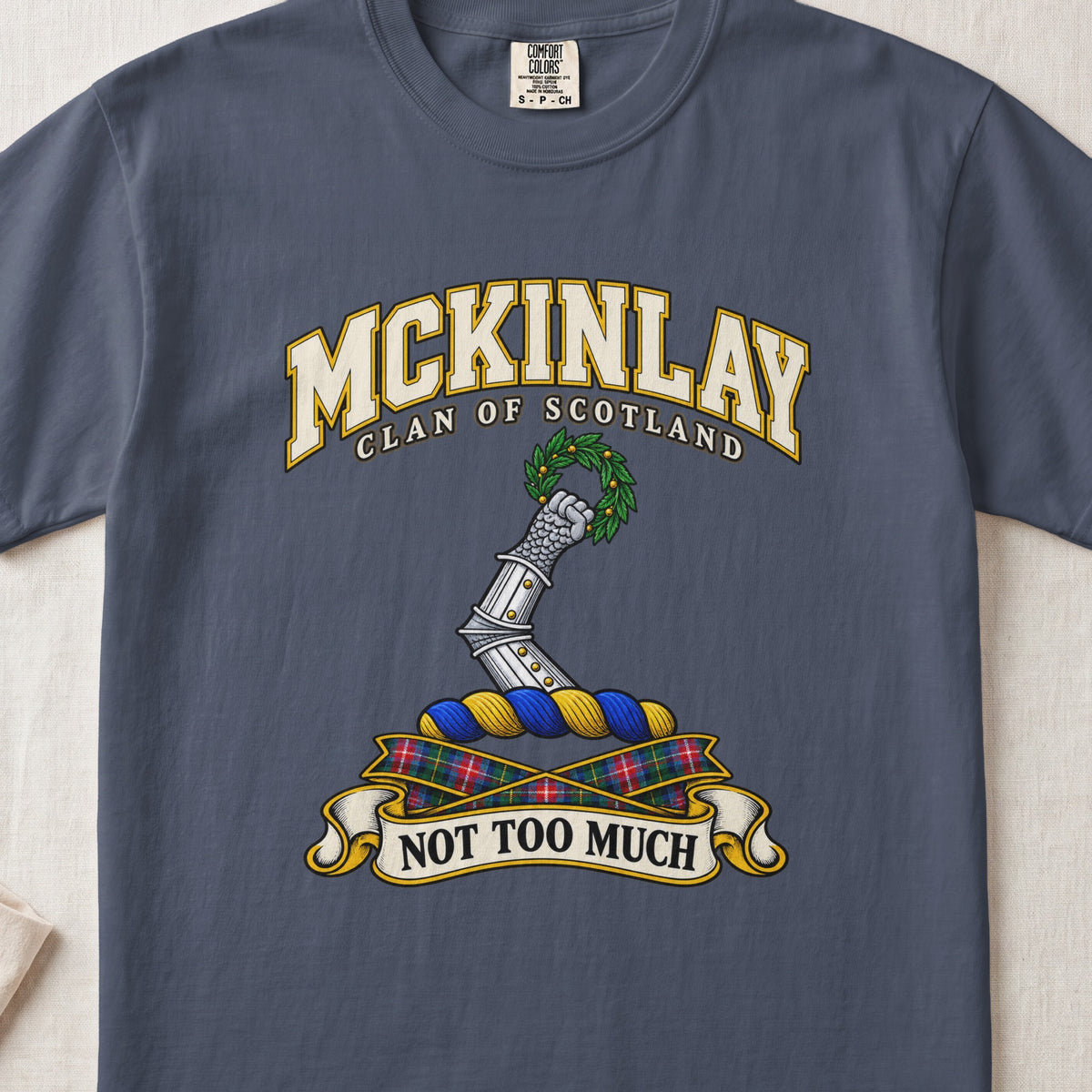 McKinlay Scottish clan T-shirt in Midnight, front view with an armored arm holding a green leafy wreath and motto banner.