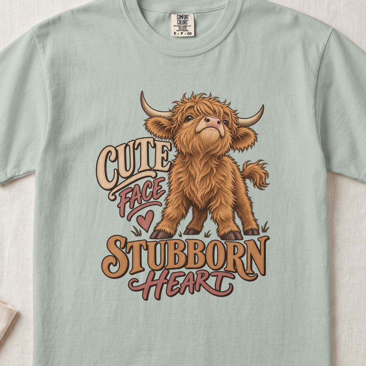 Cute Face, Stubborn Heart Highland cow design on a Bay Comfort Colors 1717 T-shirt, flat lay