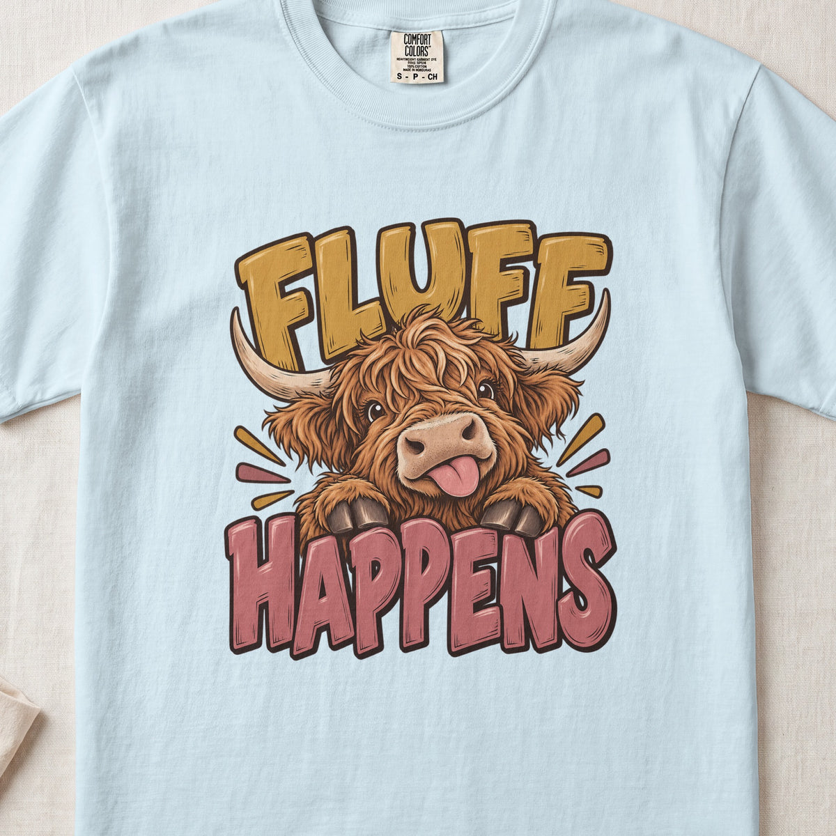 Fluff Happens Highland cow design on a Chambray Comfort Colors 1717 T-shirt, flat lay