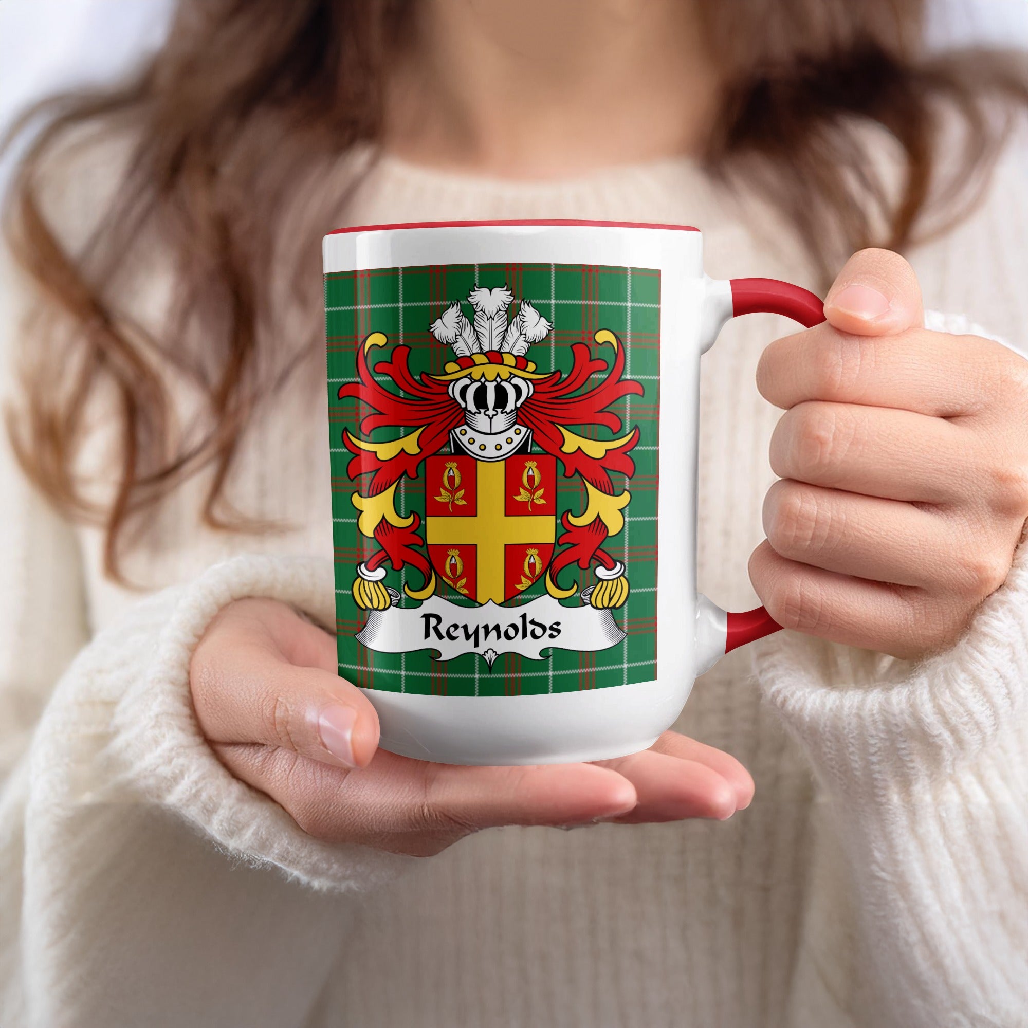Mug with Reynolds family crest on green plaid background, held by a person.