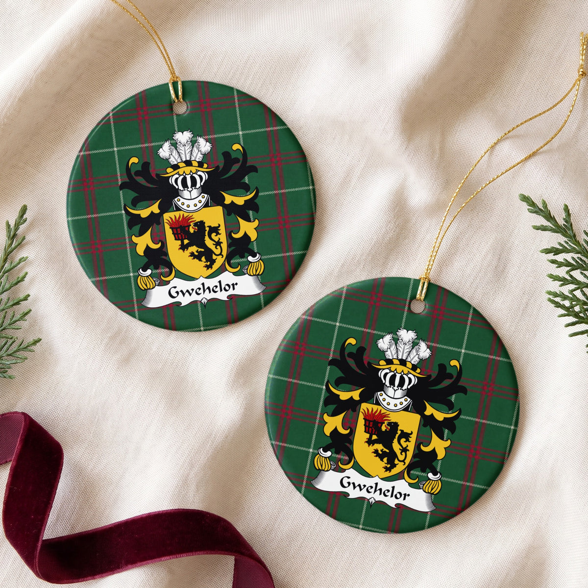 Two Gwehelor ornaments on cream fabric with evergreen and burgundy ribbon; a black lion holding a flaming basket on a gold shield on Welsh national tartan.