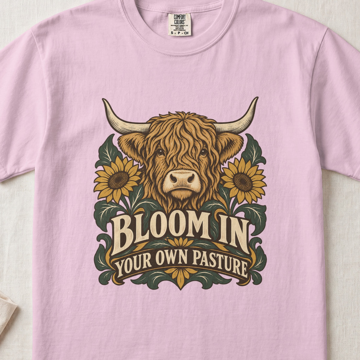 Bloom in Your Own Pasture Highland cow design on a Blossom Comfort Colors 1717 T-shirt, flat lay