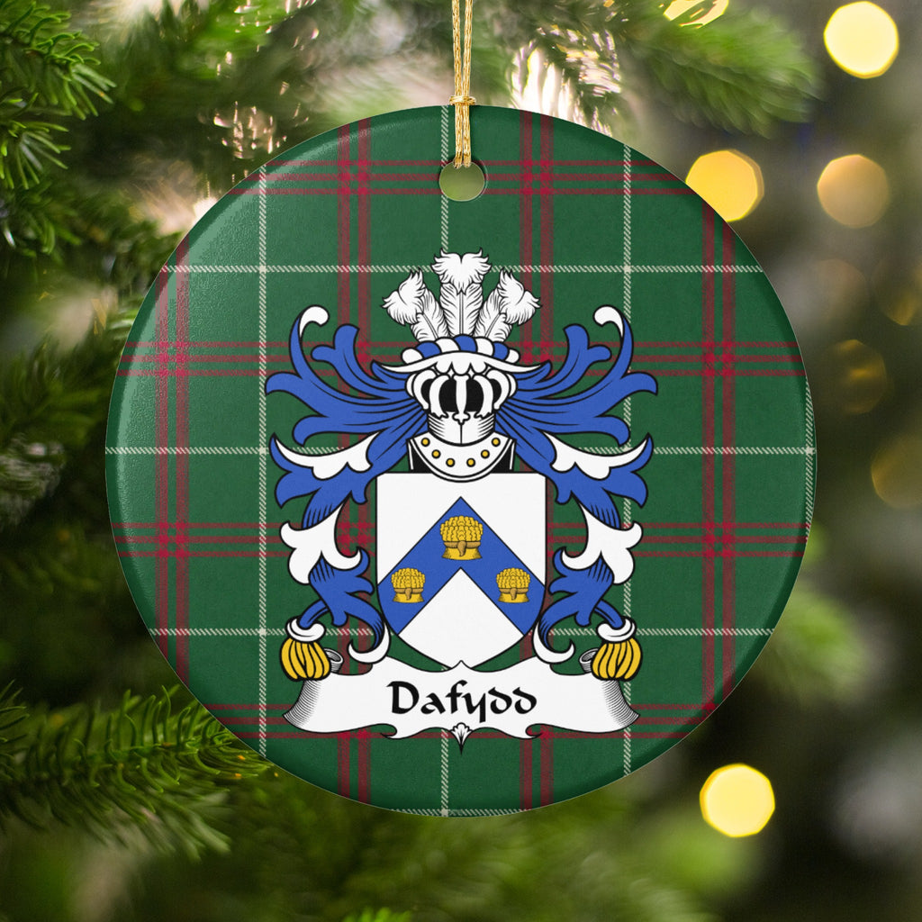 Dafydd Style 1 ornament hanging among Christmas tree branches and warm lights; a blue chevron bearing three gold wheatsheaves on a white shield on Welsh national tartan.
