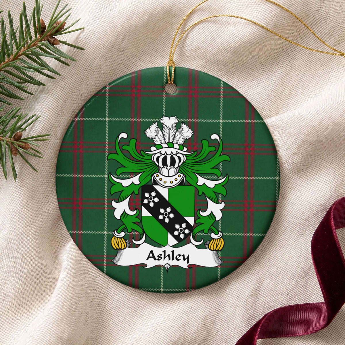 Ashley ceramic ornament with gold string on cream fabric; a green-and-white shield crossed by a black band with three white flower-like motifs on Welsh national tartan.
