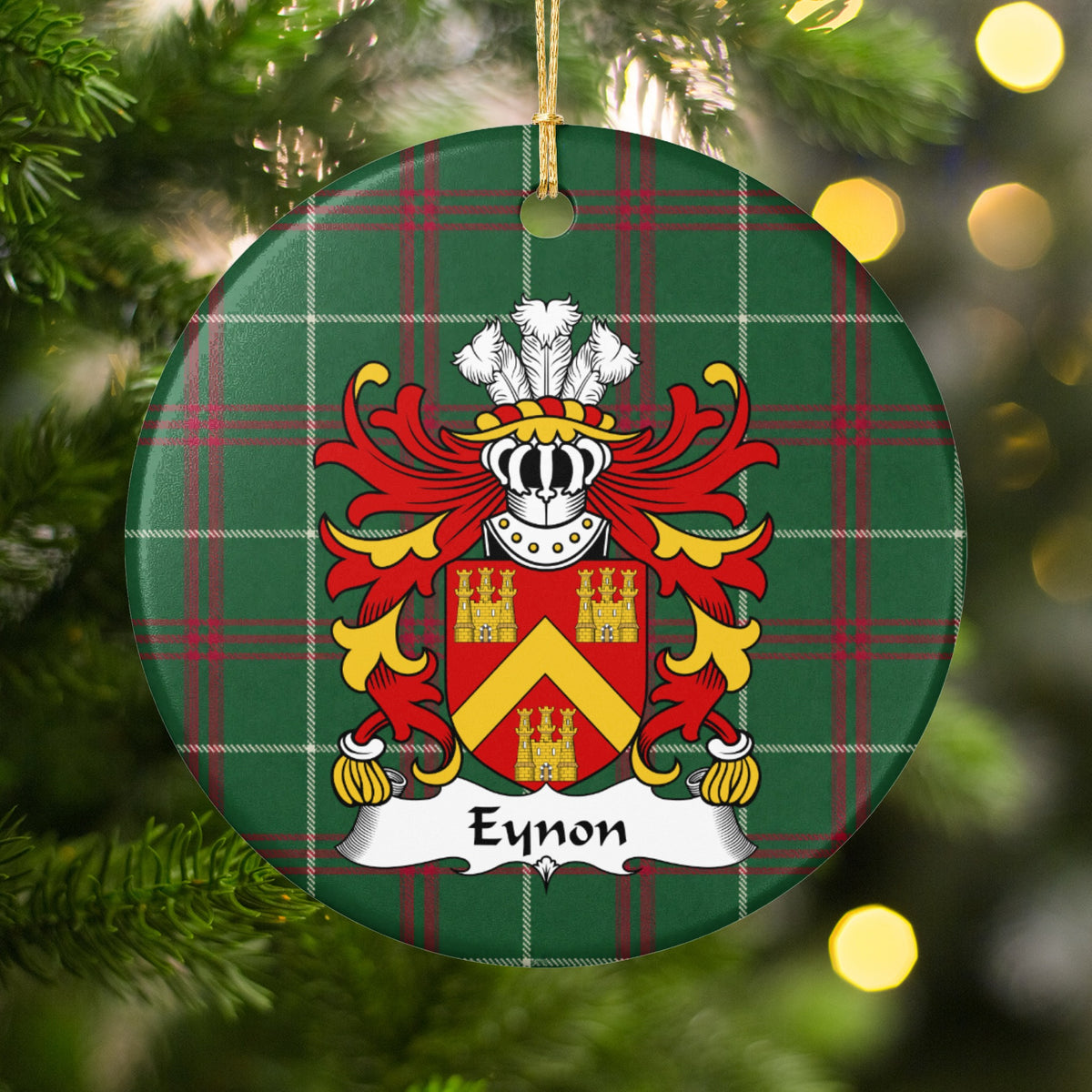 Eynon ornament hanging among Christmas tree branches and warm lights; a gold chevron between three gold castles on a red shield on Welsh national tartan.
