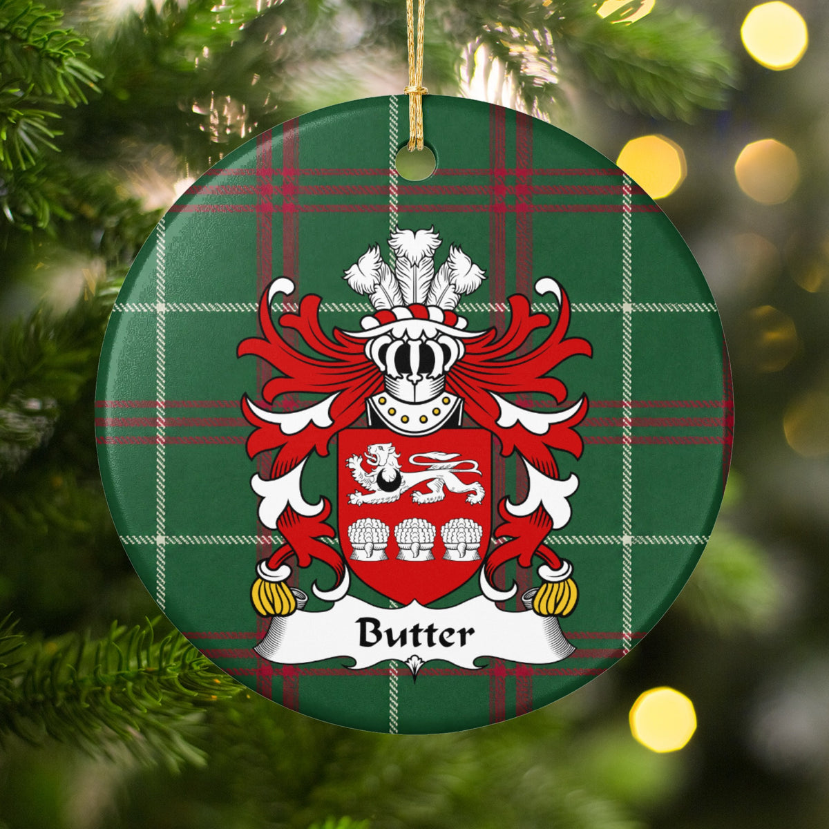 Butter ornament hanging among Christmas tree branches and warm lights; a white lion above three white wheat sheaves on a red shield, with a black crescent on the lion on Welsh national tartan.
