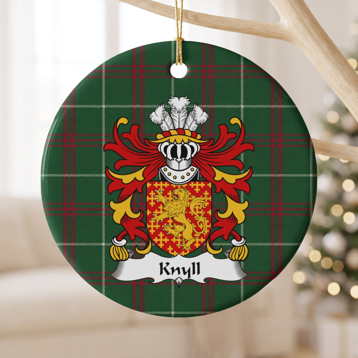 Knyll ceramic ornament hanging from a pale wooden branch, showing a red shield with a gold lion surrounded by small gold crosses on Welsh national tartan.