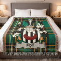 Tartan blanket with Foy crest displayed on a bed.