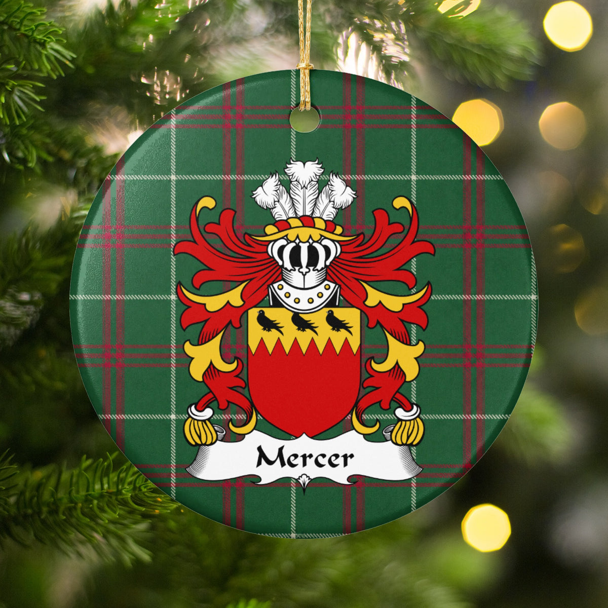 Mercer ornament hanging among Christmas tree branches and warm lights; three black birds on a jagged gold band above a red shield on Welsh national tartan.