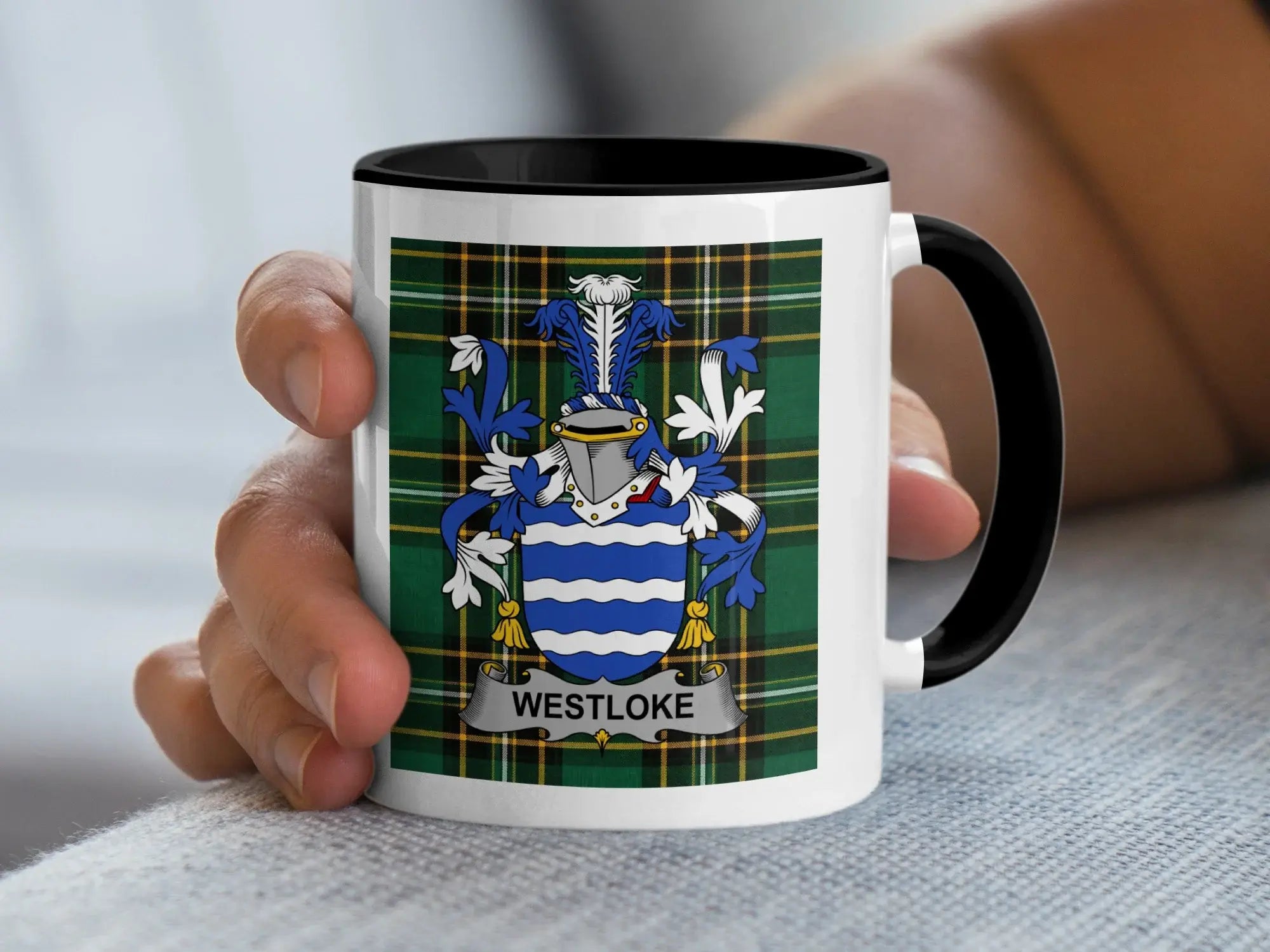 White mug with black rim displaying Westlake family crest on plaid background.