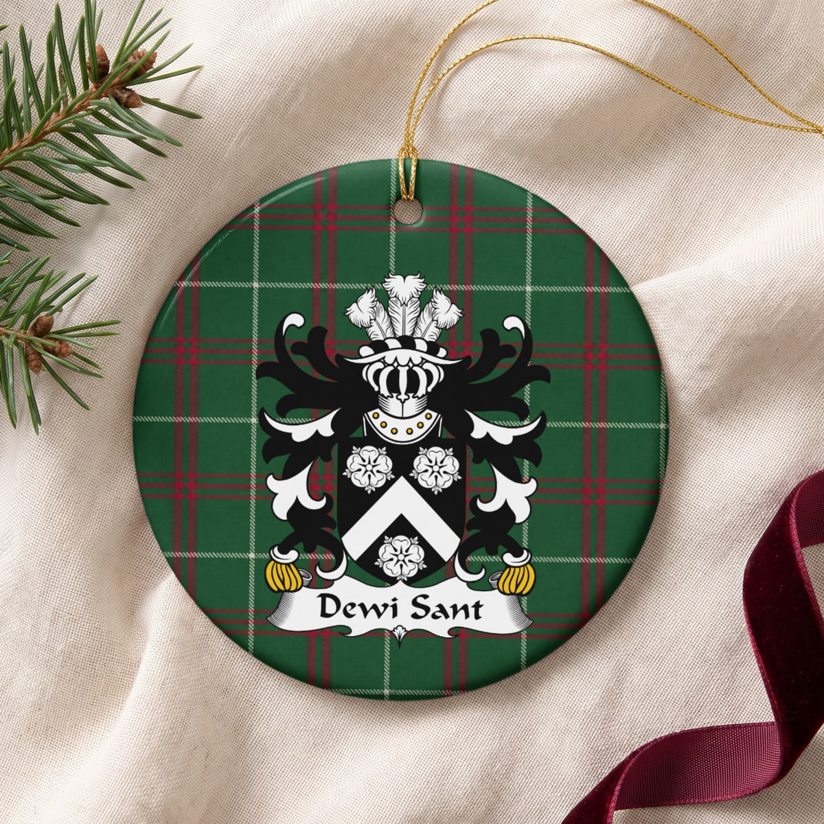 Dewi Sant ornament on cream fabric with gold string, evergreen and burgundy ribbon; a white chevron and three white roses on a black shield.
