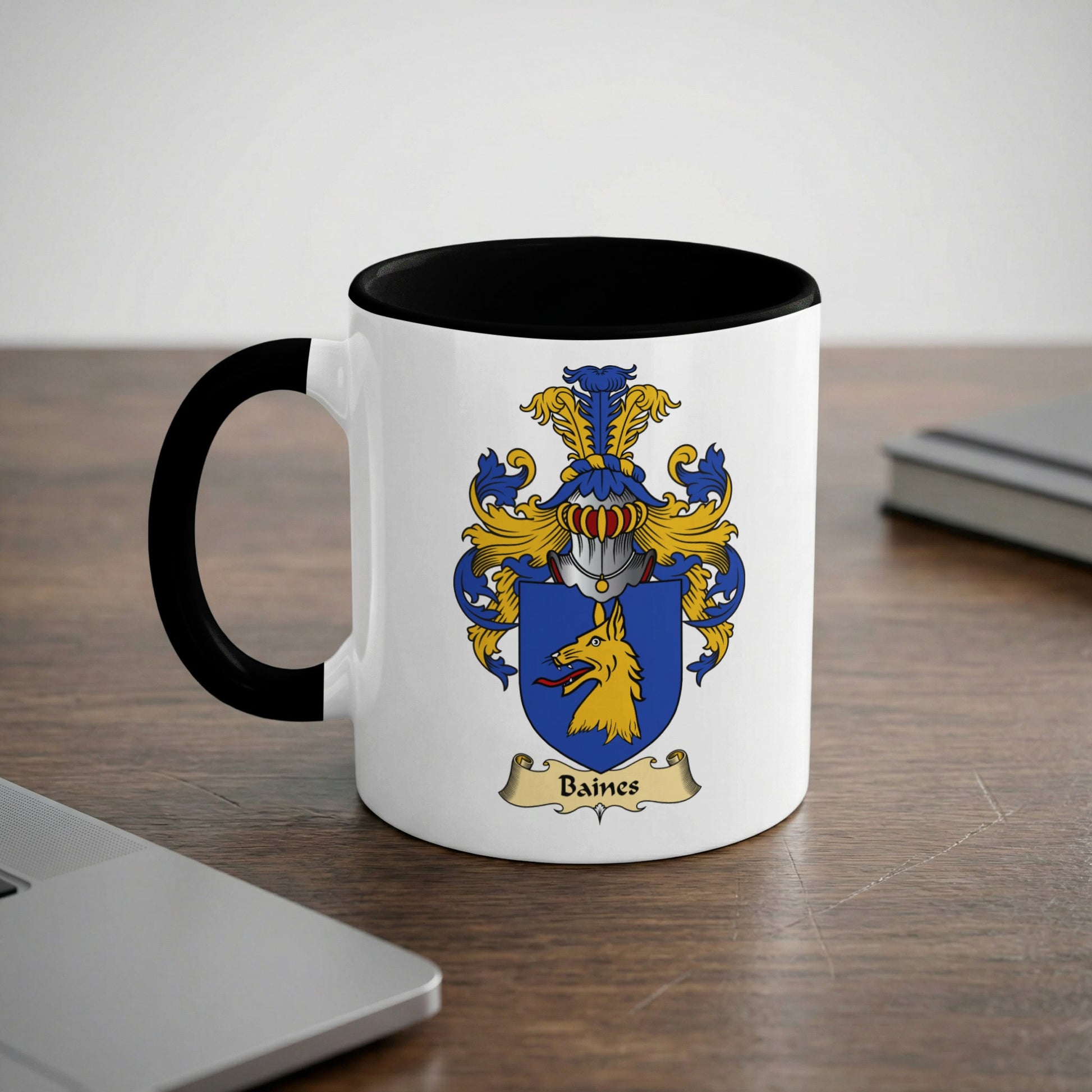 Mug with Baines family crest on a wooden desk next to a laptop.