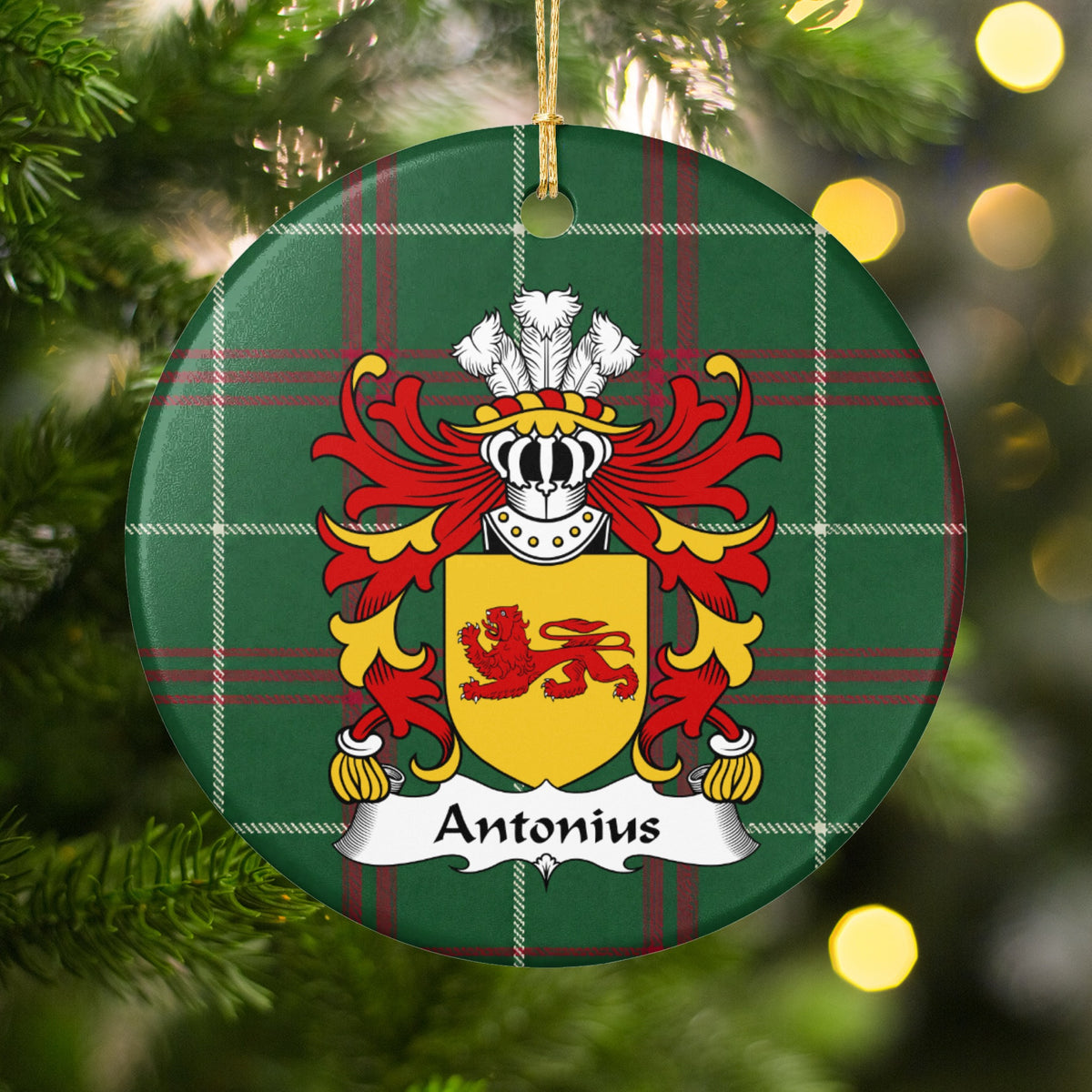 Antonius family crest and surname on a round Welsh national tartan ornament, hanging by a gold cord among Christmas tree branches and warm golden lights.