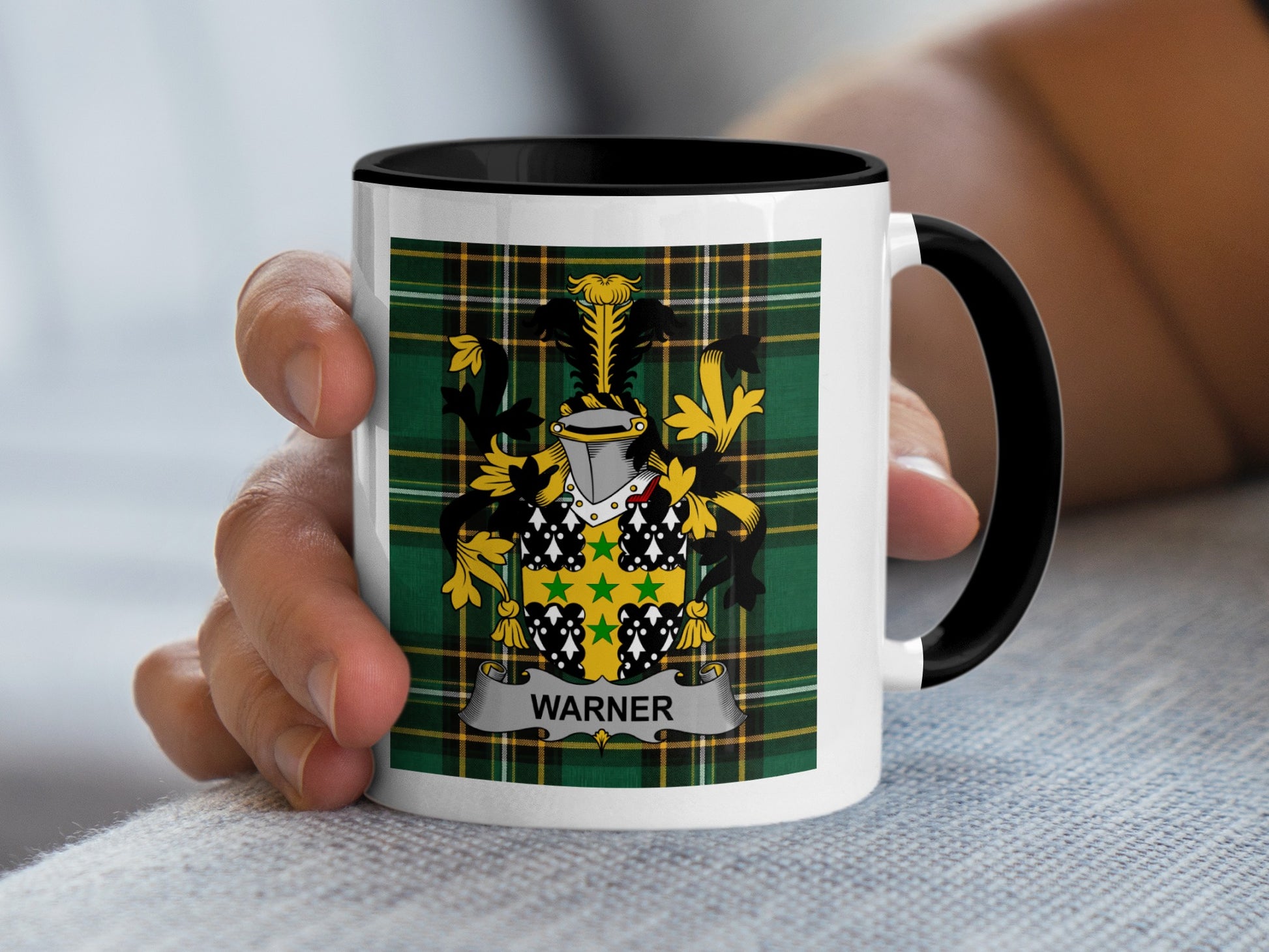 White mug with black rim displaying Warner family crest on tartan background.