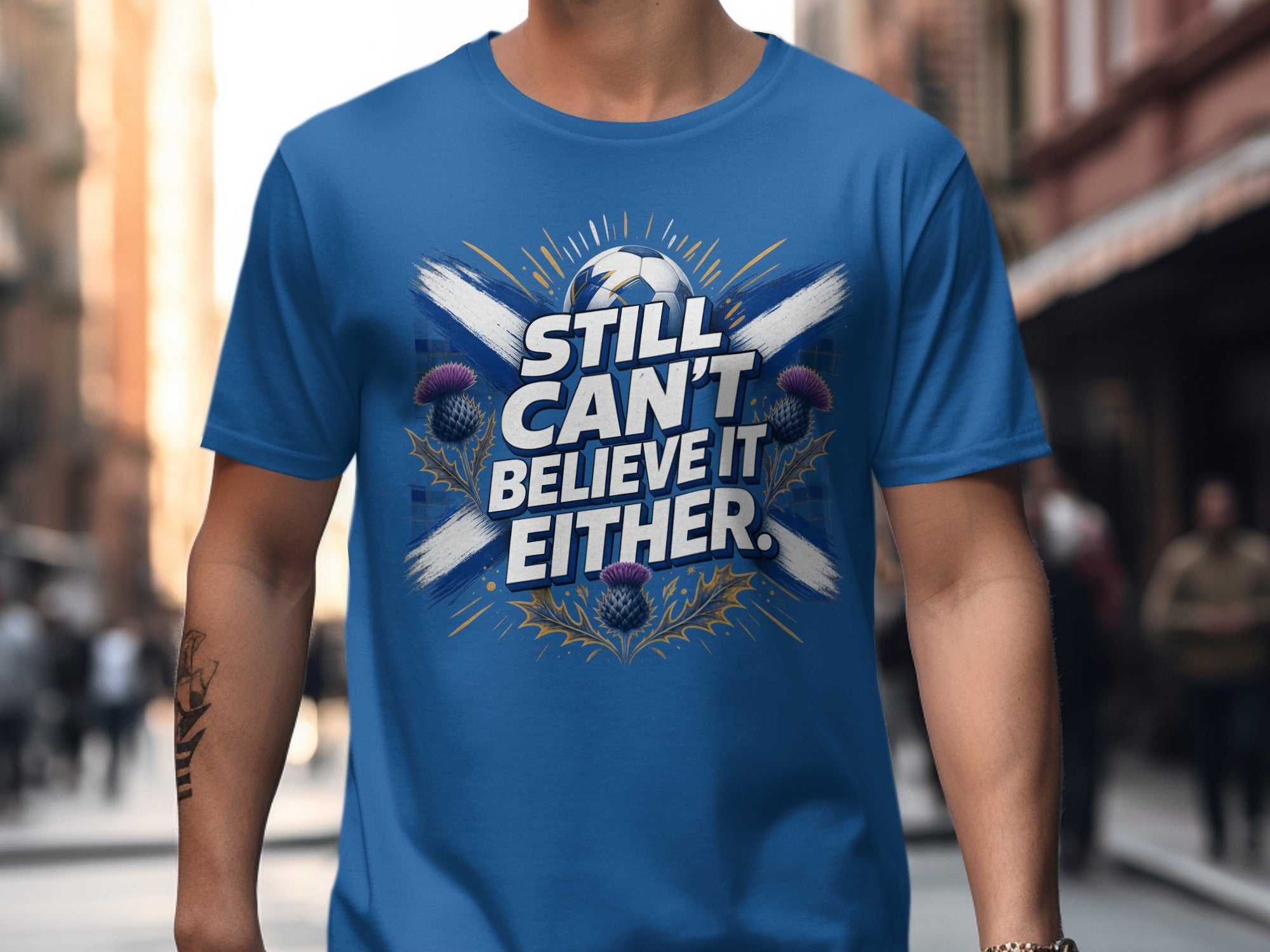 Blue t-shirt with Scottish flag, thistle, and text "STILL CAN'T BELIEVE IT EITHER."