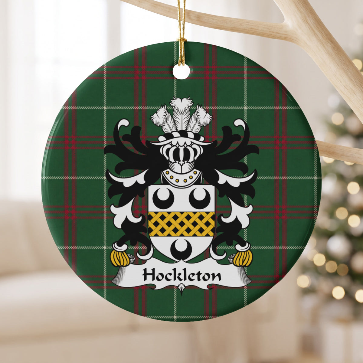 Hockleton ornament hanging from a pale wooden branch; a white shield with three black crescents and a gold lattice band on Welsh national tartan.